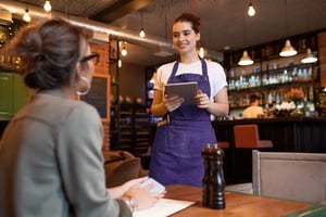Kellnerin nimmt Bestellungen mit der FoodGenius Restaurantsoftware am Tisch auf und kassiert Gäste ab.